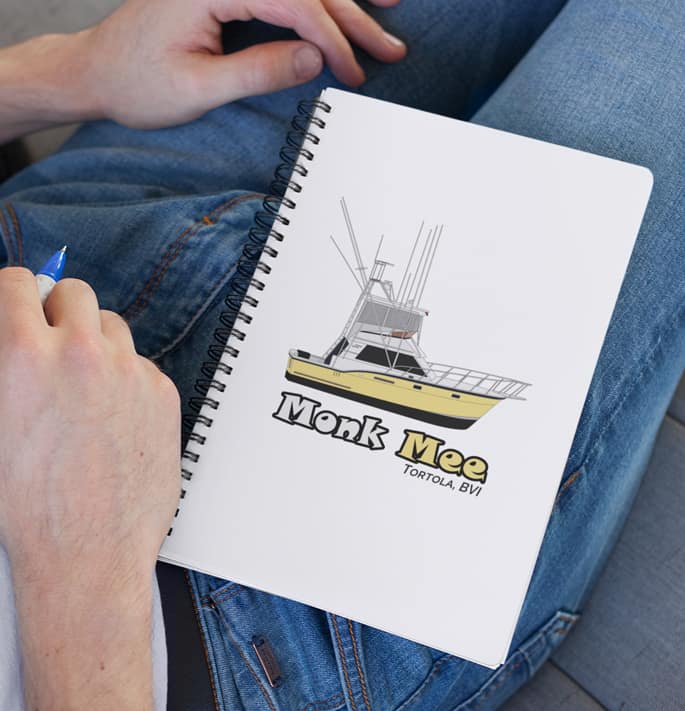An image of a custom spiral notebook with boat art on a person's lap.