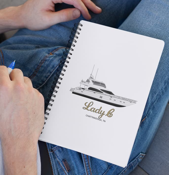 An image of a custom spiral notebook with boat art on a person's lap.