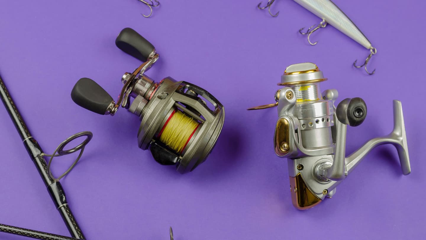 Baitcast and Spinning reels sitting side by side next to lures and fishing rods. 